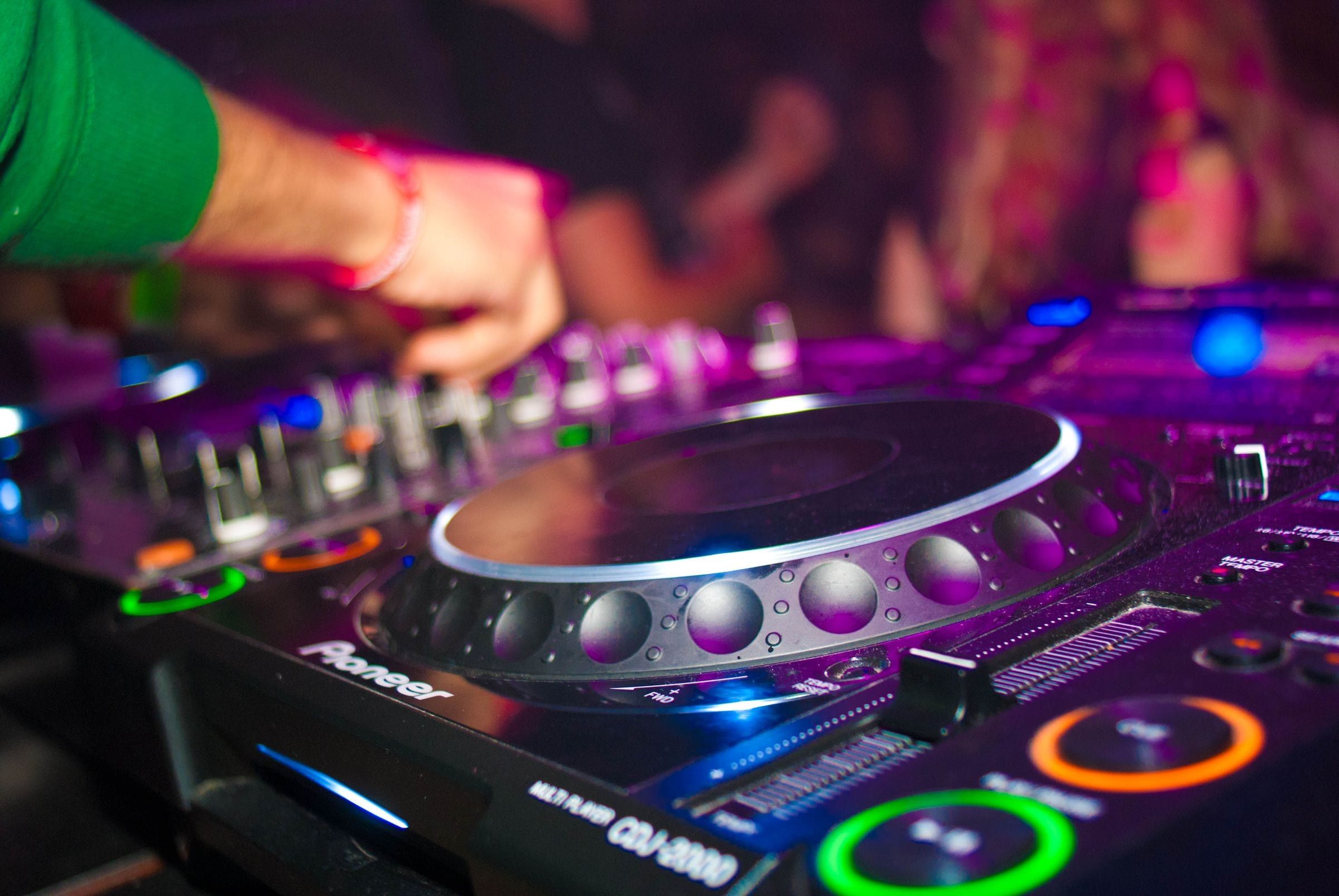 Hands on a DJ mixing console under colourful party lighting