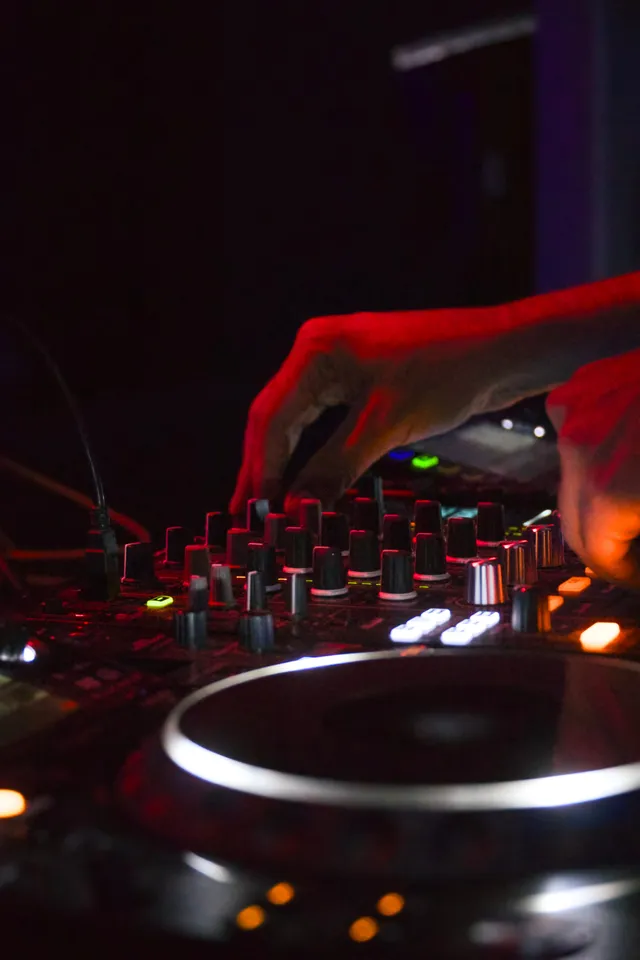 Hands working a DJ mixer under warm red club lighting
