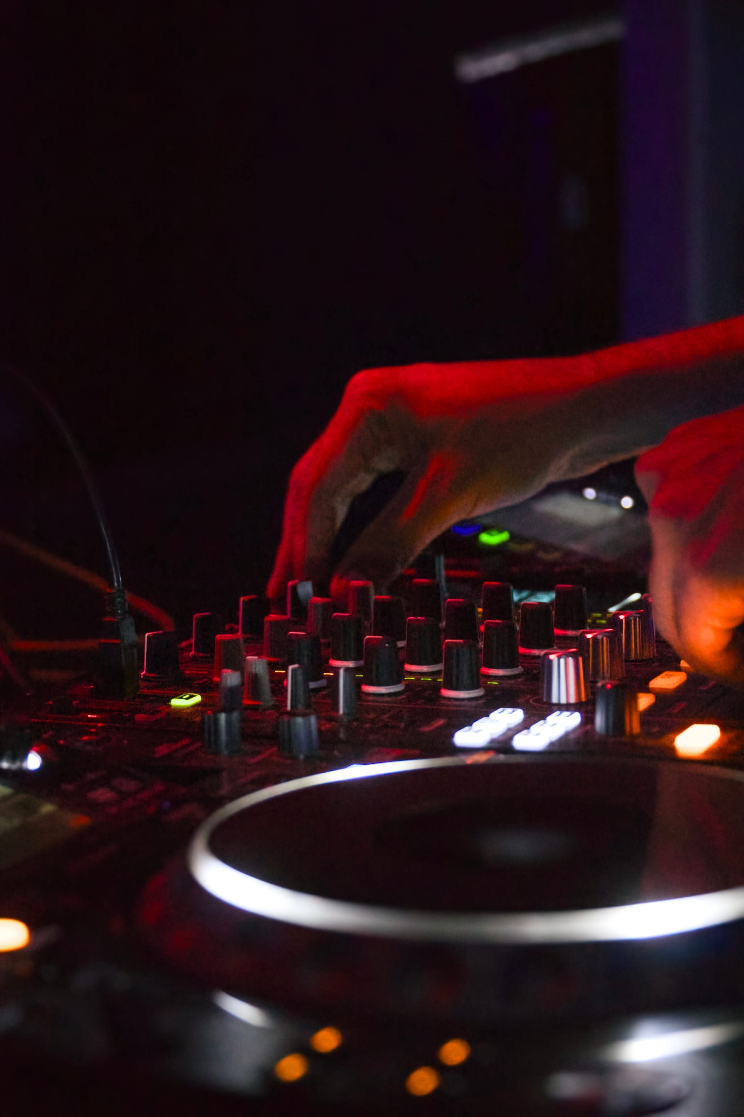 Hands working a DJ mixer under warm red club lighting