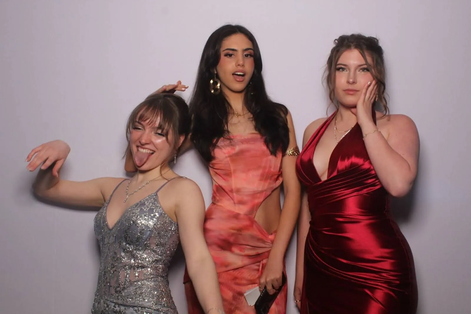 Three guests in formal dresses posing and pulling faces against a plain white photo booth backdrop.