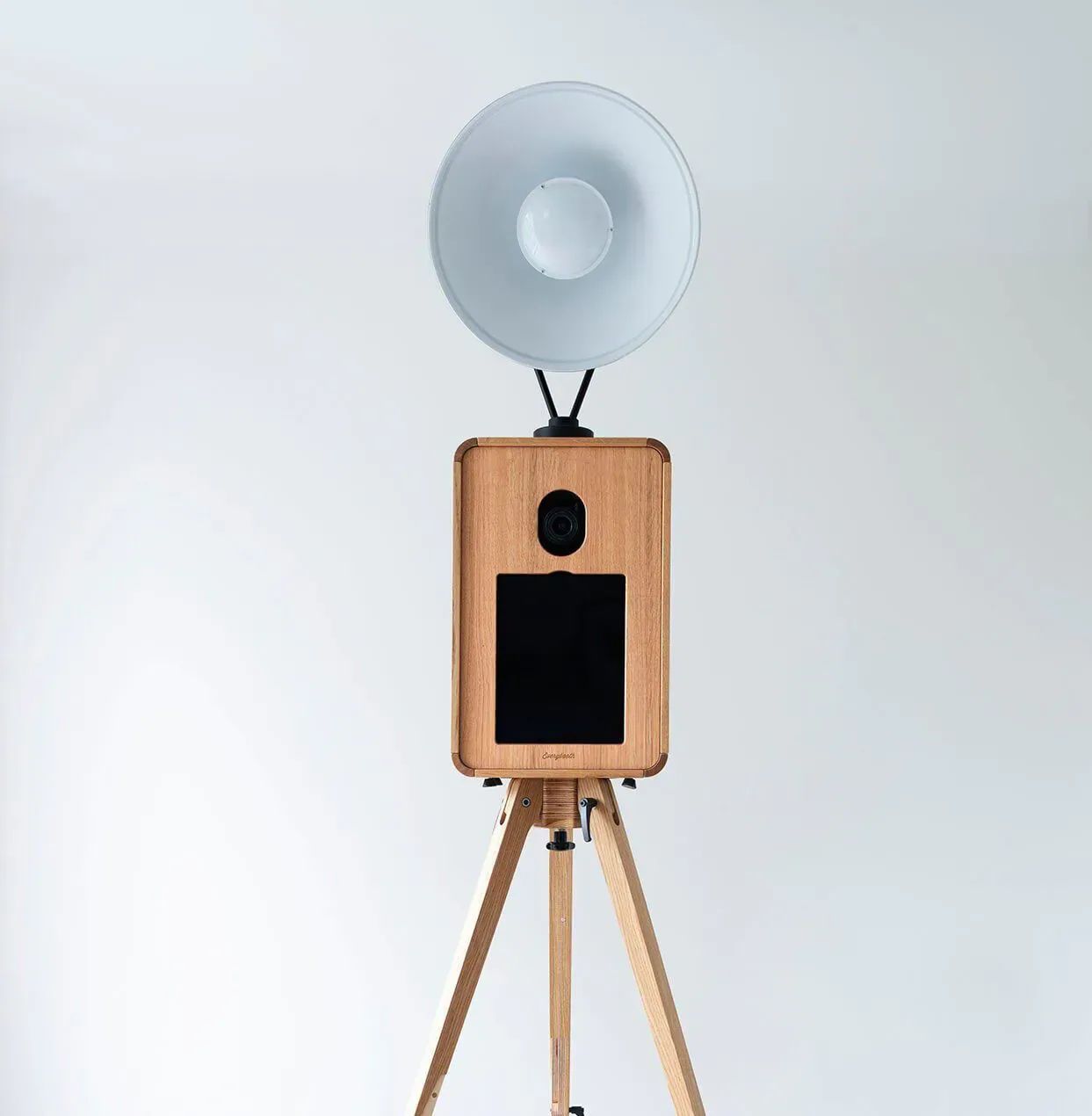 Glam photo booth: a wooden-framed booth with a large ring light on a wooden tripod, against a plain studio backdrop.