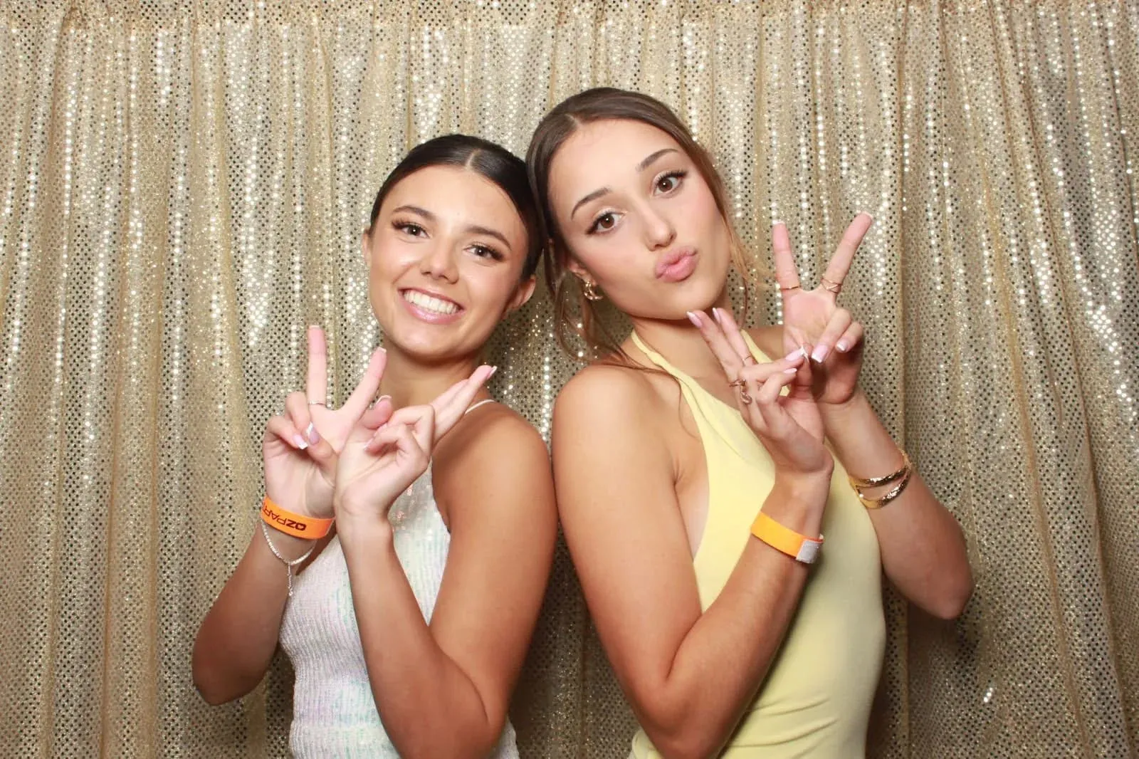 Two guests pulling peace signs in front of a gold sequin backdrop.