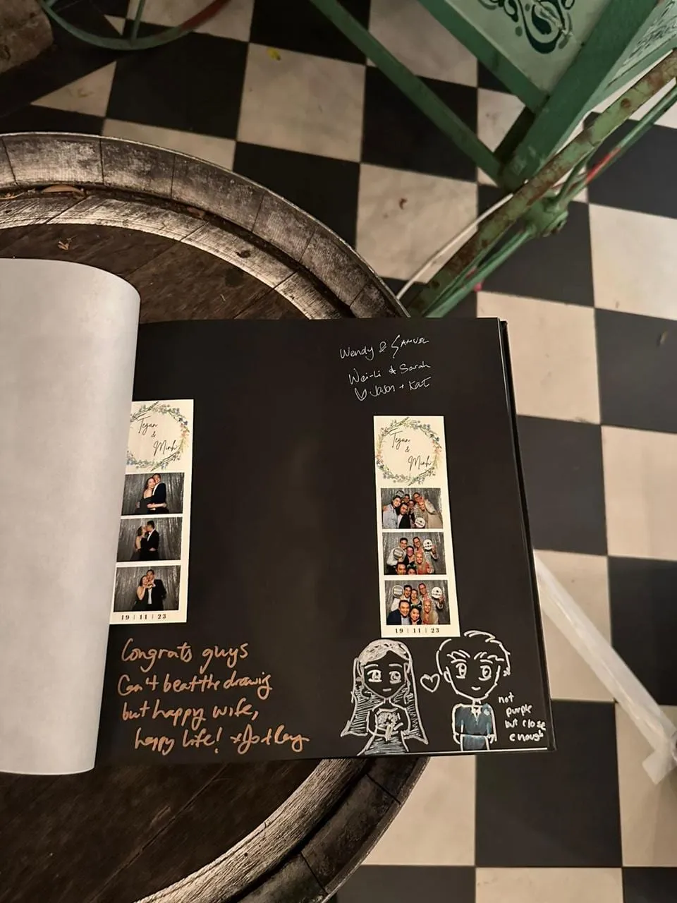 An open guest book on a wine barrel showing photo booth strips alongside handwritten messages and a drawing.