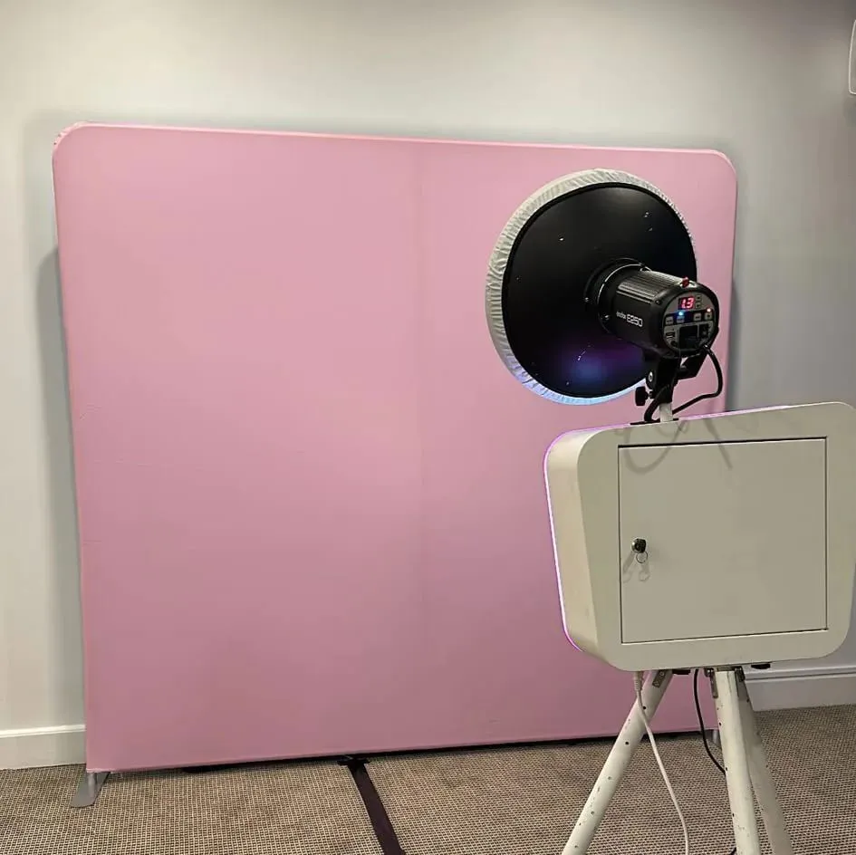 Open-air photo booth on a tripod with a ring flash set up in front of a pink tension backdrop.